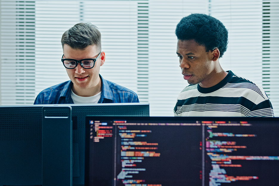 IT experts develop and analyze cloud applications across multiple monitors displaying lines of program code.