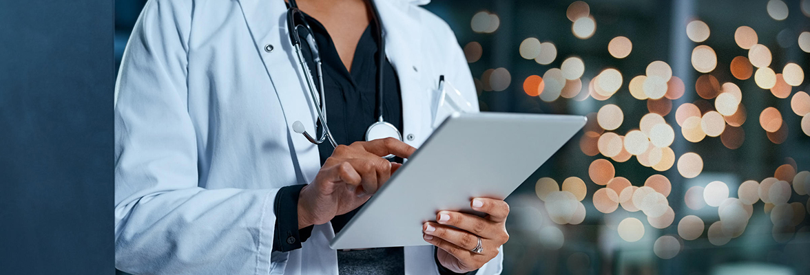 Ärztin oder Arzt in weißem Kittel nutzt ein Tablet, im Hintergrund unscharfe Lichter