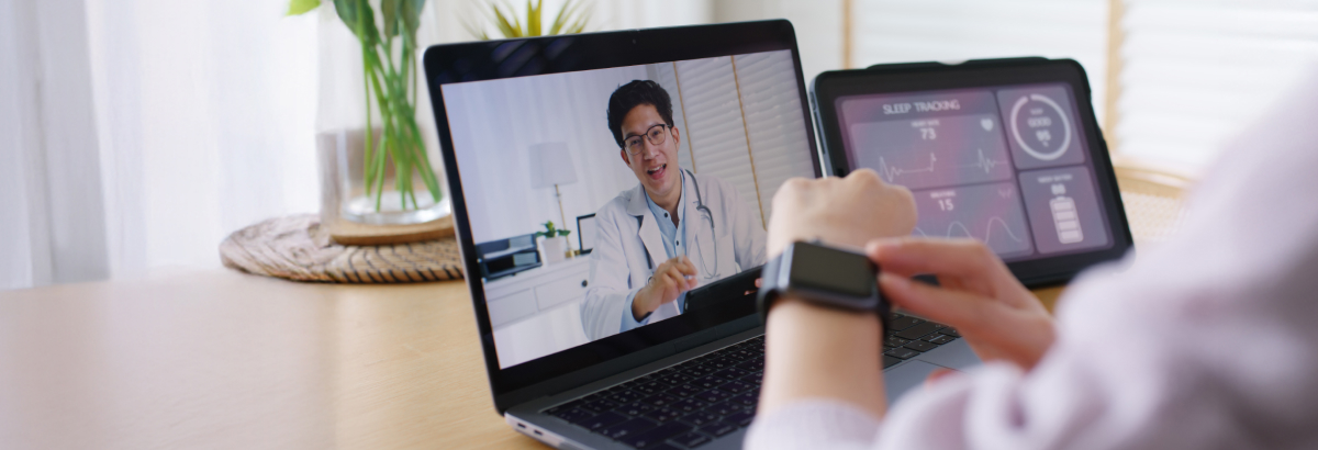 A person wearing a smartwatch sits in front of a laptop and receives online advice from a doctor.